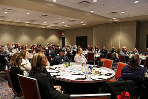 A large group of people sitting around a number of tables listening to a presentation