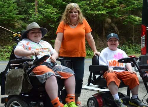 a woman posing with two children in wheelchairs