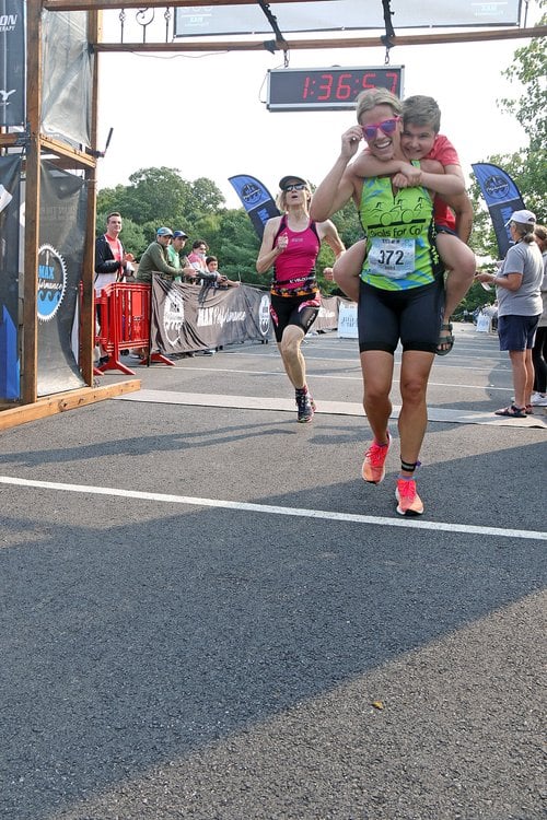 triathlon runner crossing the finish line carrying someone on their back