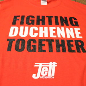 red t-shirt with fighting duchenne together text, fighting and together are written in black, duchenne written in white, jett logo written in white underneath